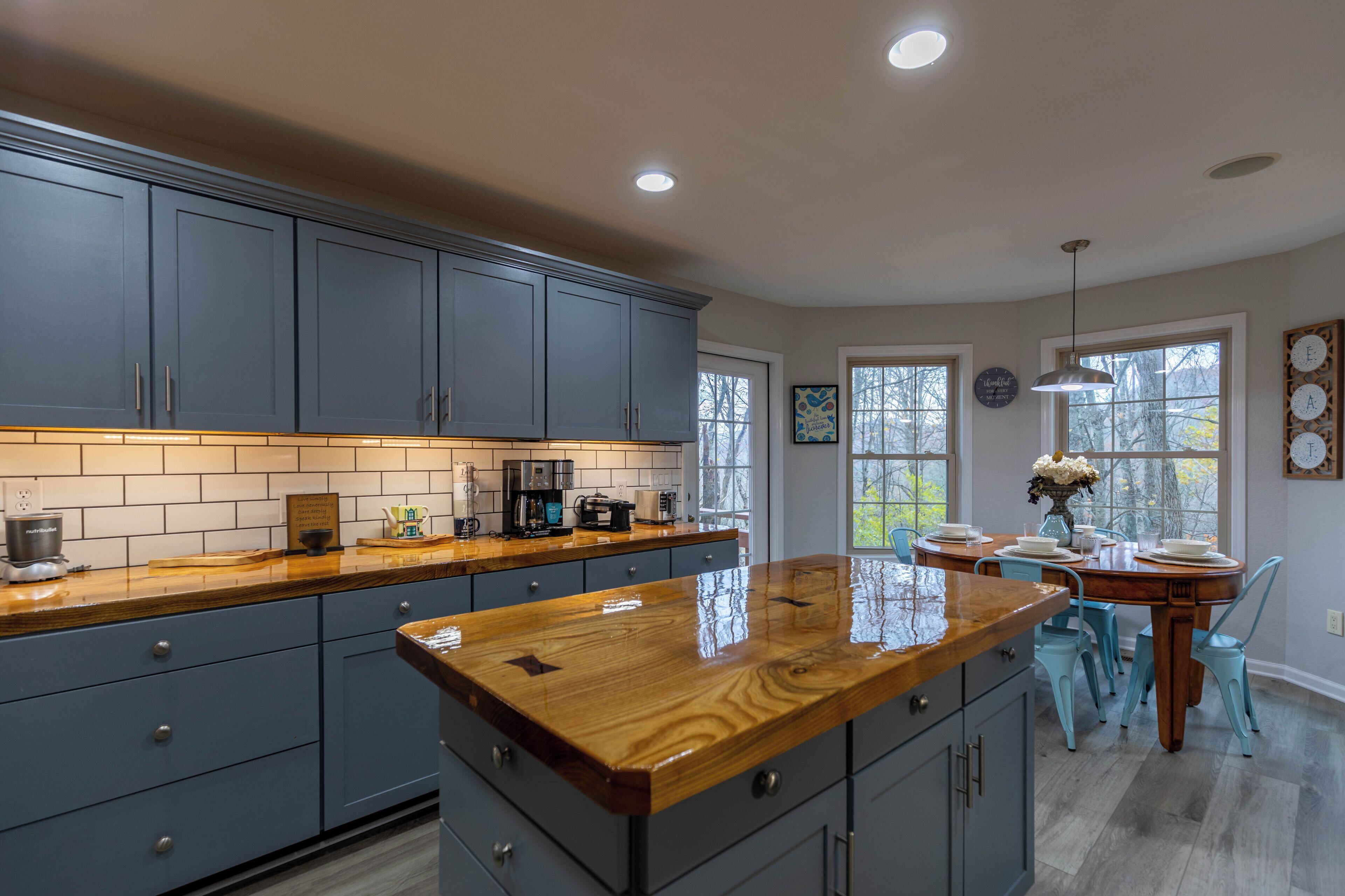 A kitchen with grey cabinets, a wooden countertop, and a dining area with a table and chairs.