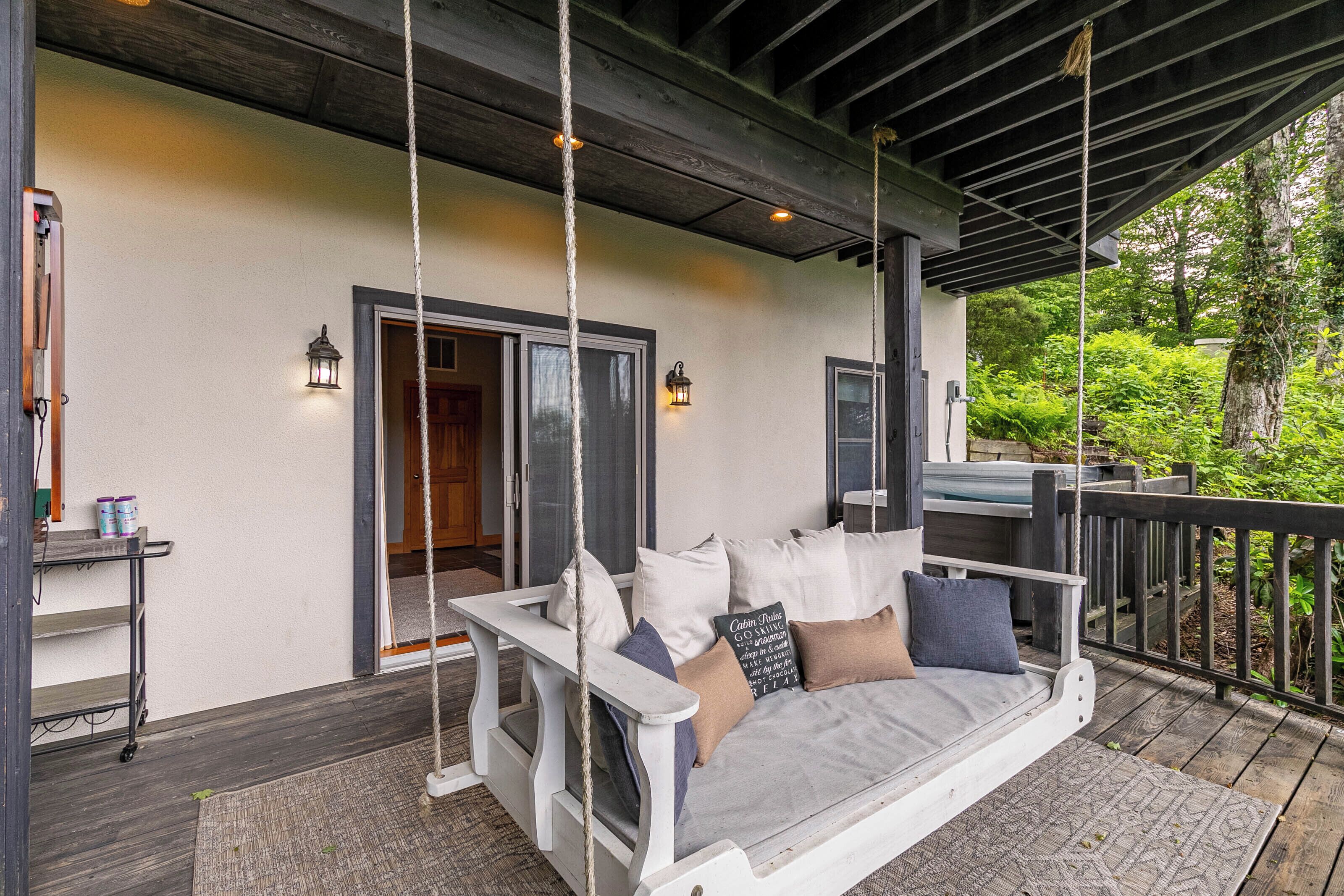 A wooden deck with a white swing seat, a small table with paint cans, and a door leading inside.