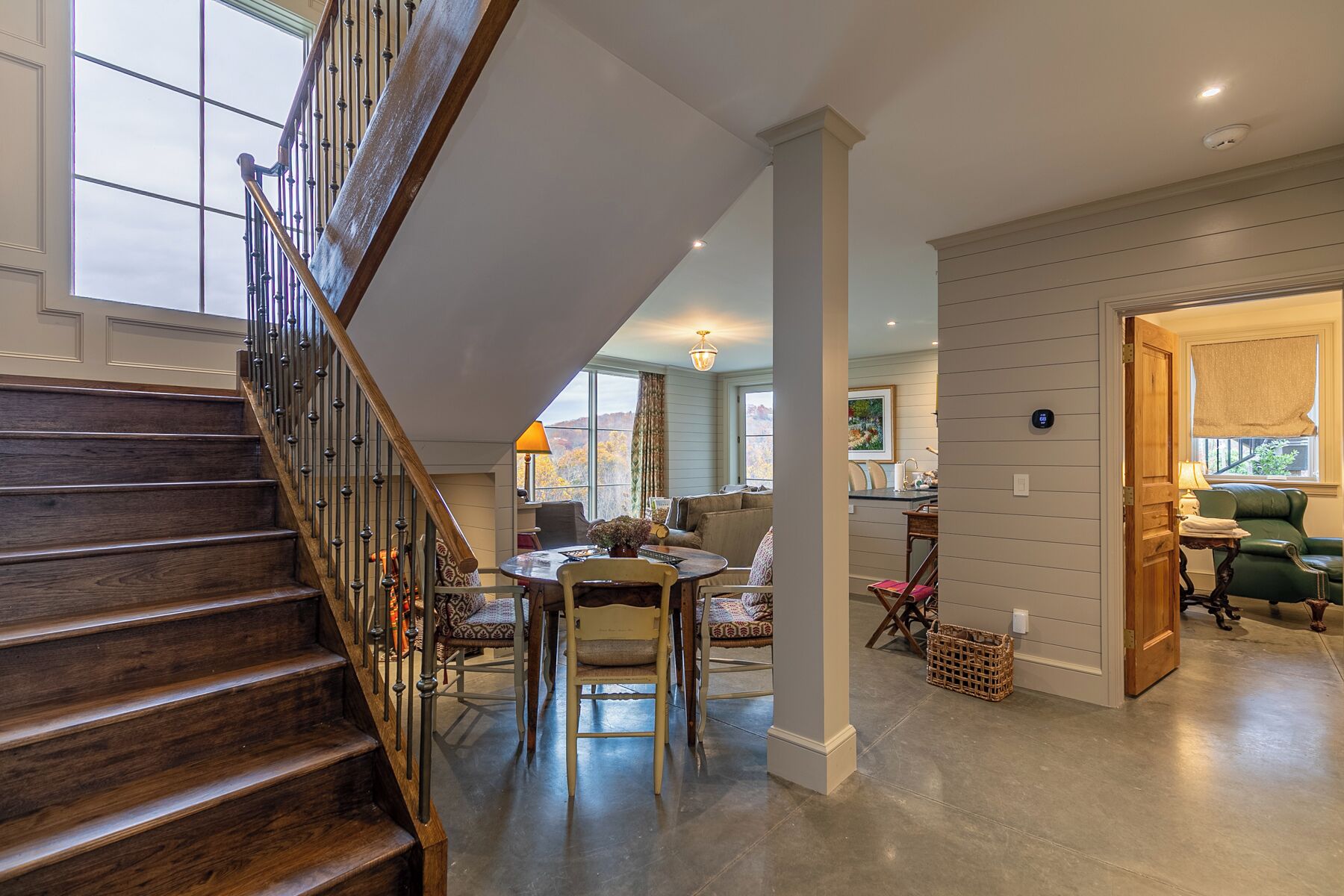 A spacious living area with a wooden staircase, a dining table, and a view of the outdoors.