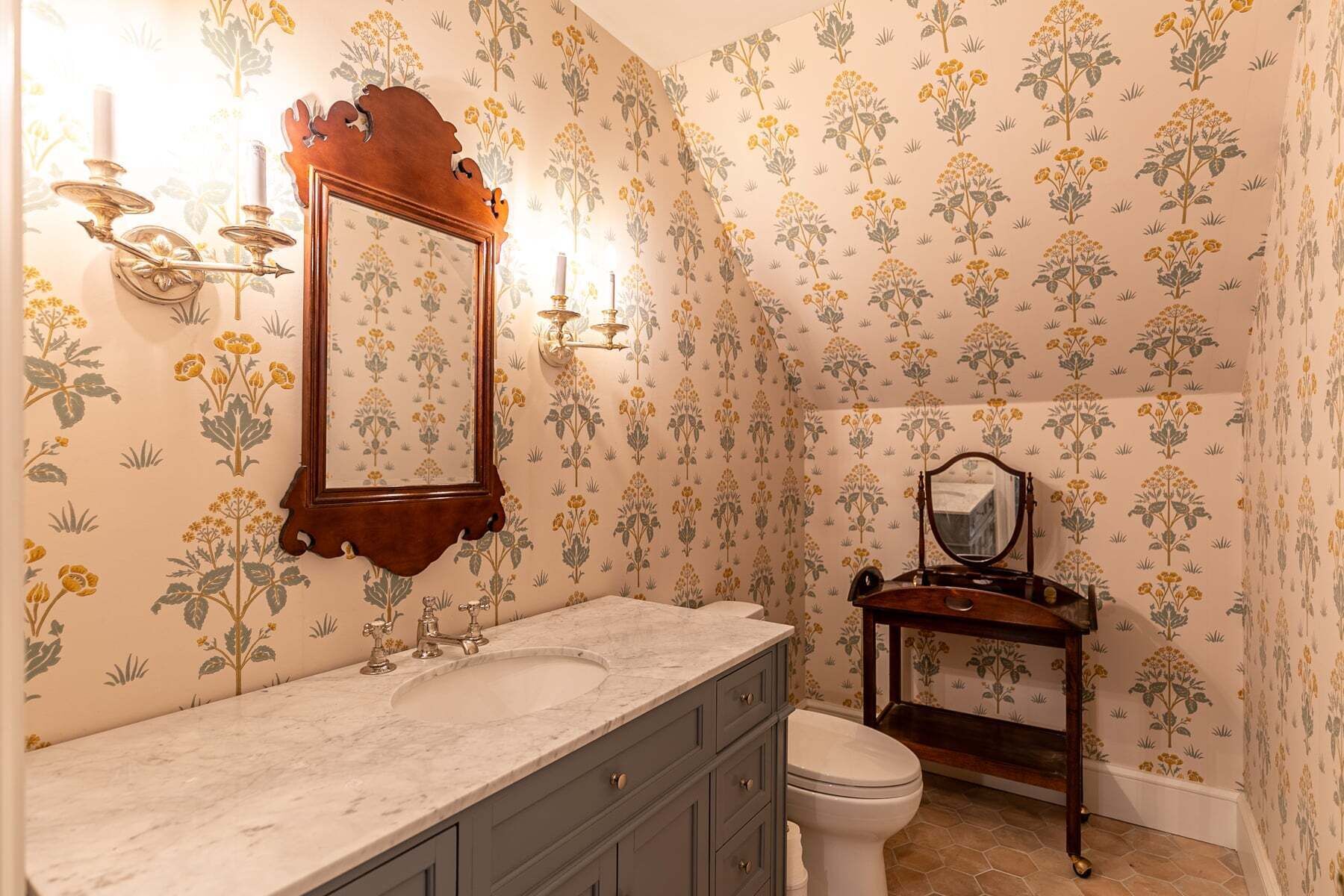 A bathroom with a marble sink, a wooden vanity, a mirror, and a toilet.