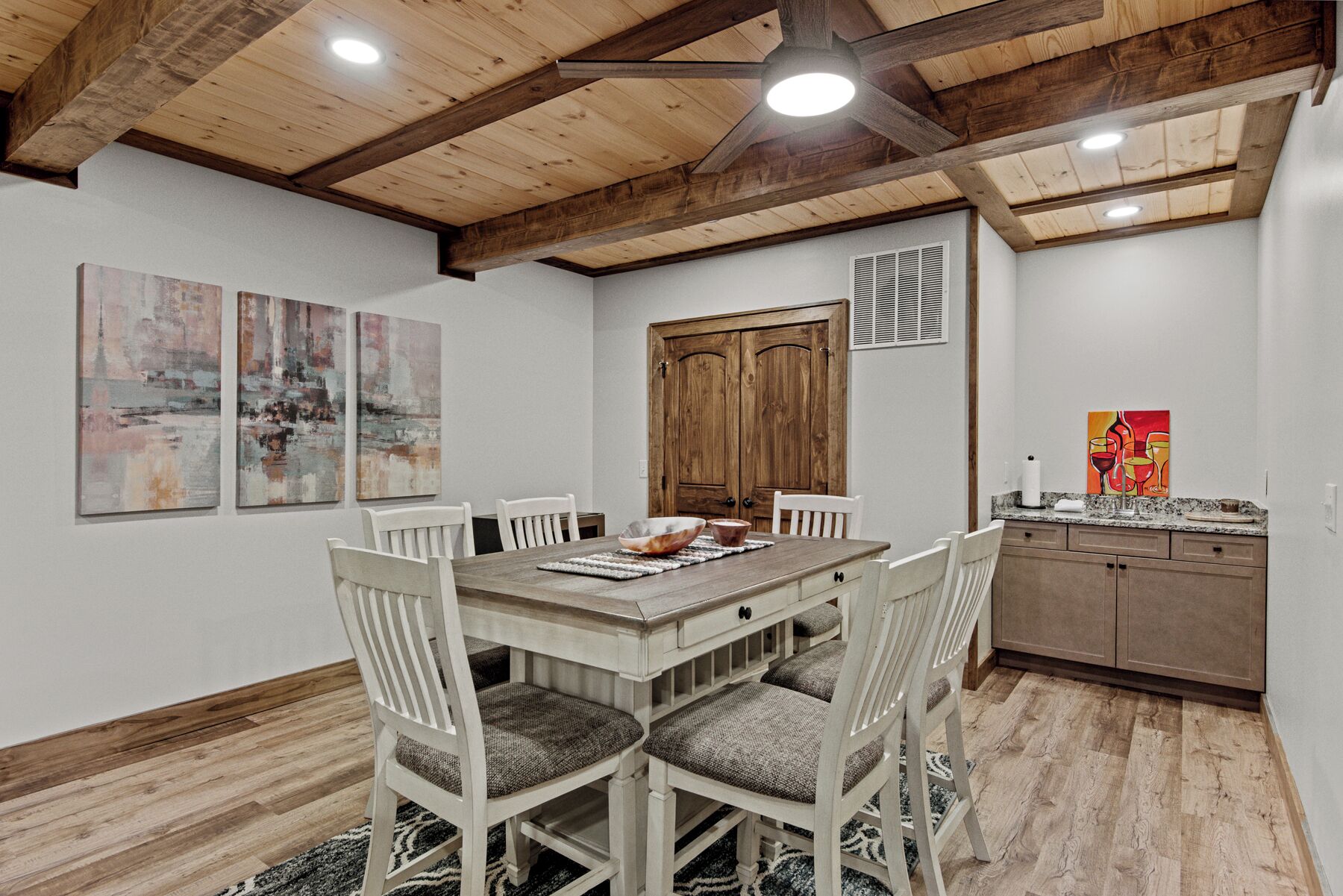 A dining area with a wooden table and chairs, a wooden ceiling with exposed beams, and artwork on the walls.