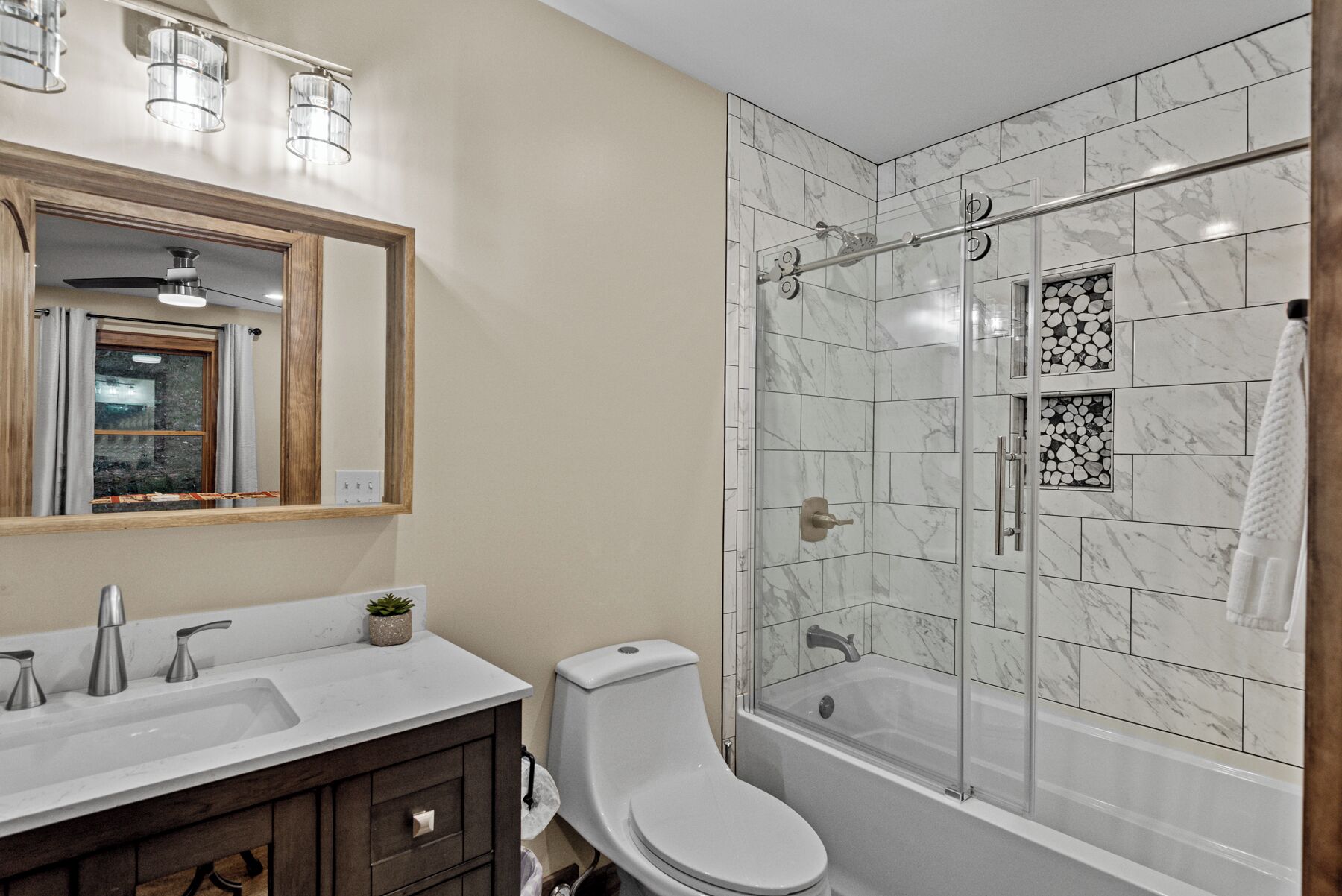 A bathroom with a shower, toilet, sink, and mirror.