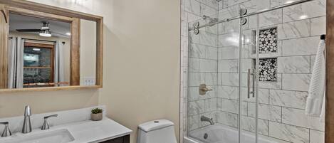 A bathroom with a shower, toilet, sink, and mirror.