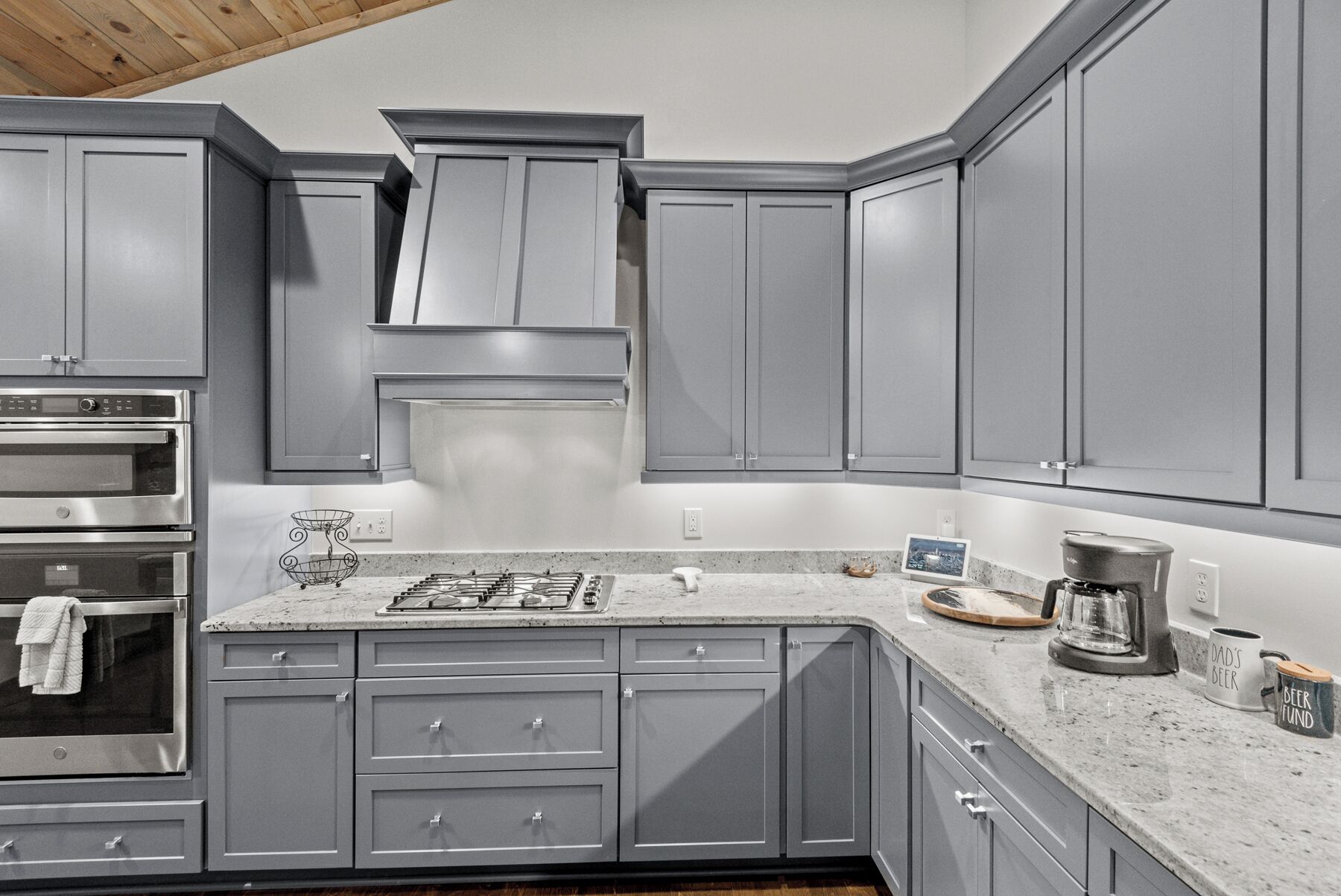 A modern kitchen with grey cabinets, a built-in oven, a gas stove, and a coffee maker.