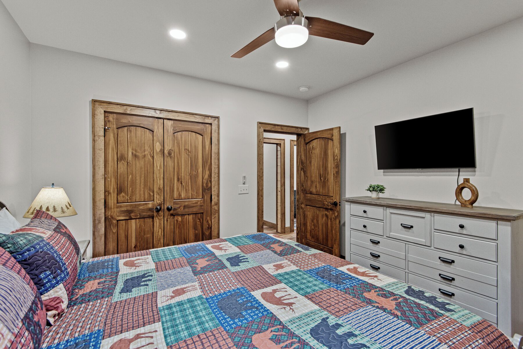 A bedroom with a bed, a dresser, a television, and wooden doors.