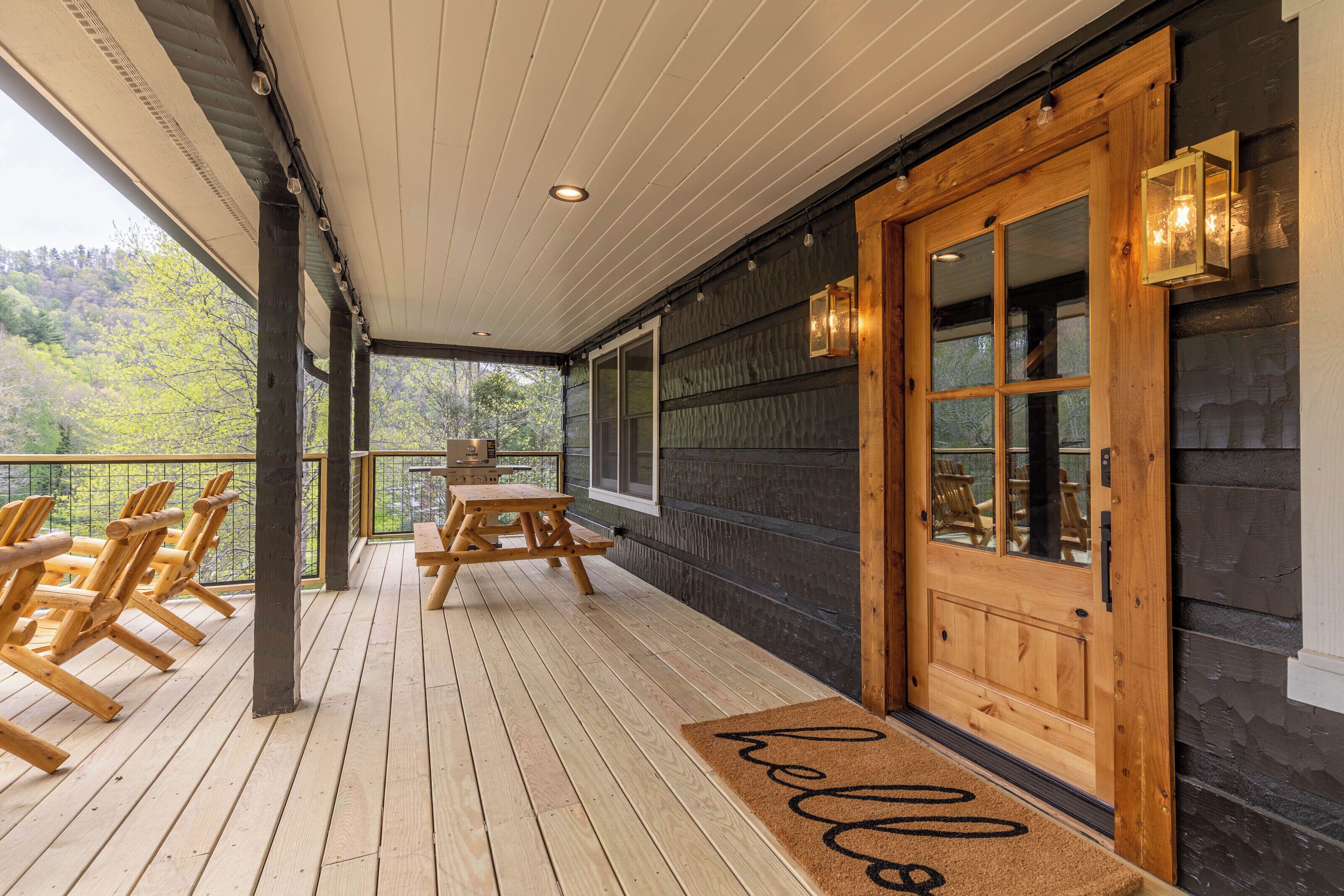 A wooden deck with a bench and chairs, a wooden door with glass panels, and a view of trees.