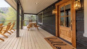 A wooden deck with a bench and chairs, a wooden door with glass panels, and a view of trees. - River Run Cabin - Watauga River in Valle Crucis With Firepit, Pet Friendly, Oversize Deck (Sugar Grove)