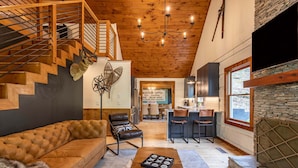 A modern interior with a staircase, leather furniture, a dining area, and a stone fireplace. - River Run Cabin - Watauga River in Valle Crucis With Firepit, Pet Friendly, Oversize Deck (Sugar Grove)