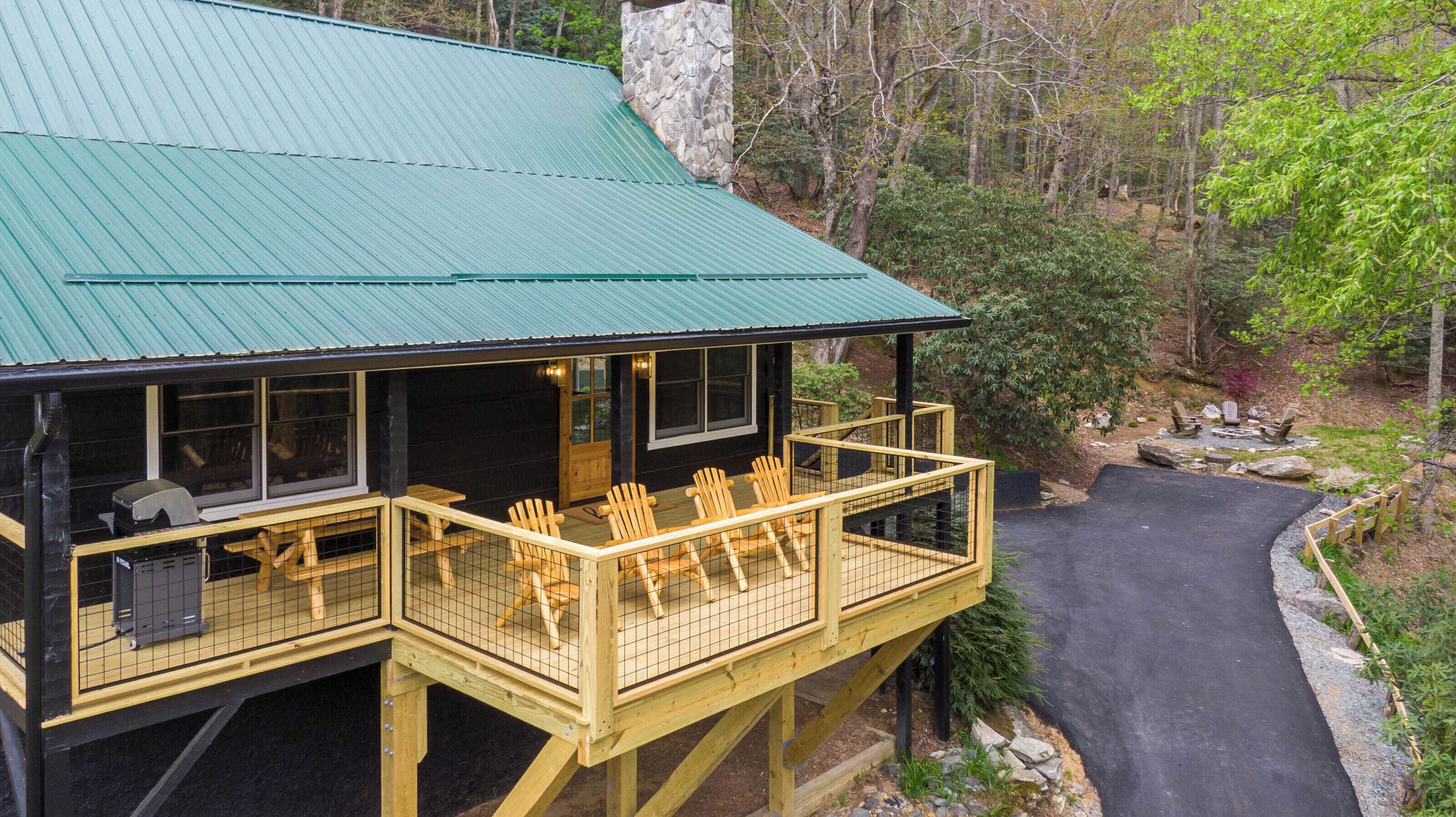 A cabin with a green roof, wooden deck, and outdoor seating area.