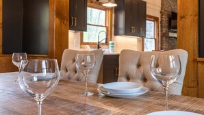 A dining table with four wine glasses and plates, a wooden table, and dark wooden cabinets in a cozy kitchen setting. - River Run Cabin - Watauga River in Valle Crucis With Firepit, Pet Friendly, Oversize Deck (Sugar Grove)