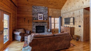 Een blokhut van binnen met een stenen open haard, houten wanden, een televisie en een gezellige zithoek.
