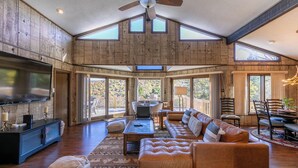 A spacious living room with a large TV, leather sofas, a ceiling fan, and large windows. - Hawk Haven (Banner Elk)