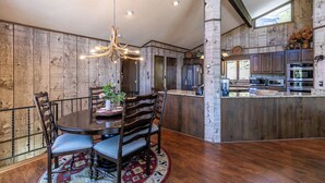 A dining area with a round table, chairs, a chandelier, and a kitchen with modern appliances. - Hawk Haven (Banner Elk)