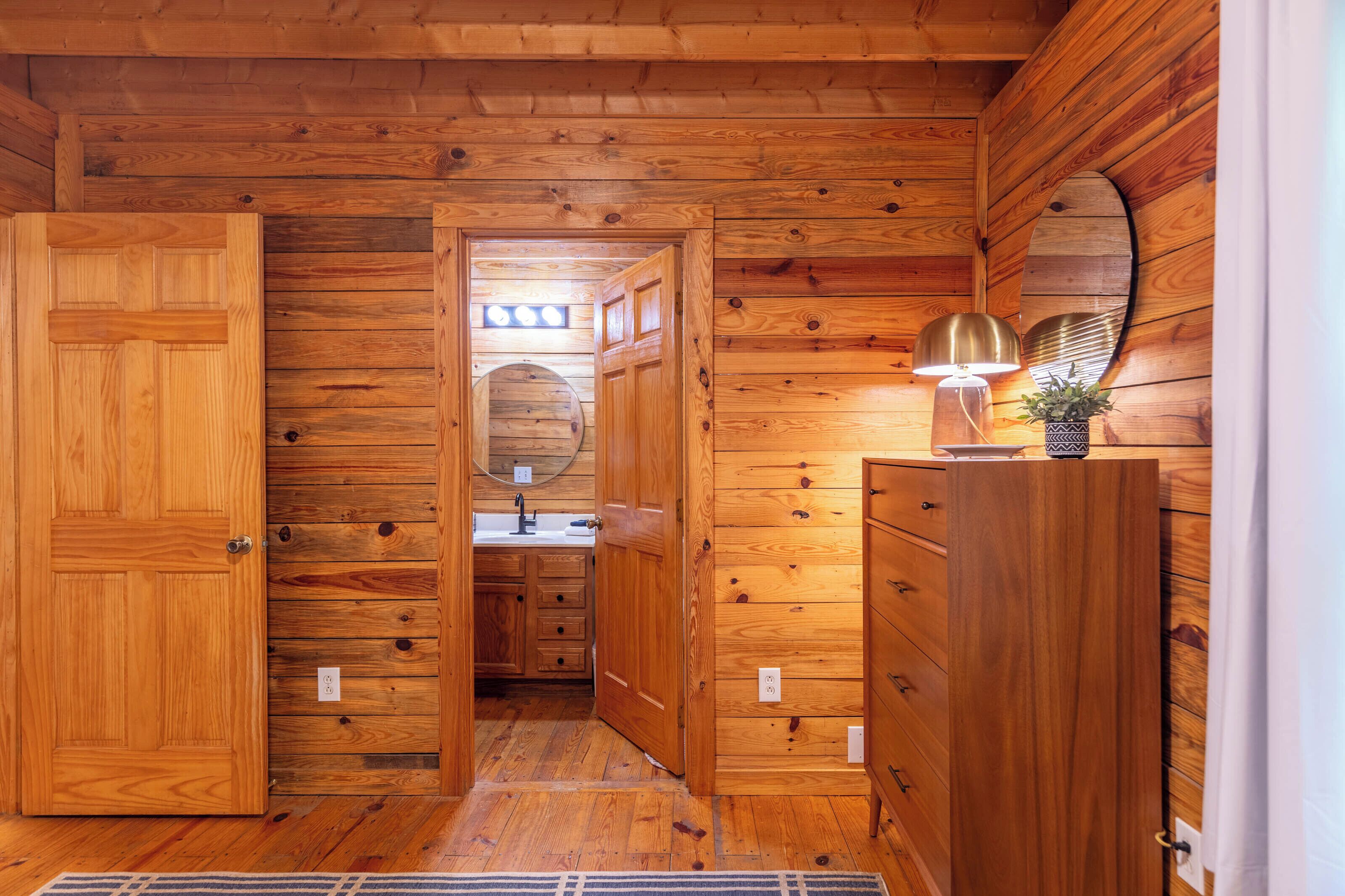 A wooden-paneled room with a door, a mirror, a dresser, and a lamp.