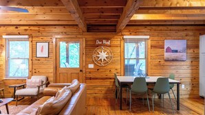 Interior de una cabaña de madera con comedor, sofá y una brújula fijada a la pared.