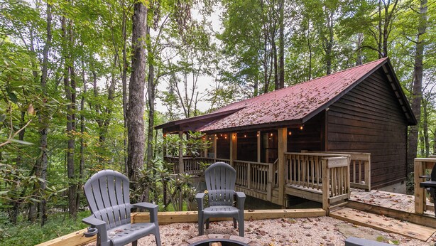 Una cabaña con terraza, rodeada de árboles, con un hoyo de fuego y sillas Adirondack.