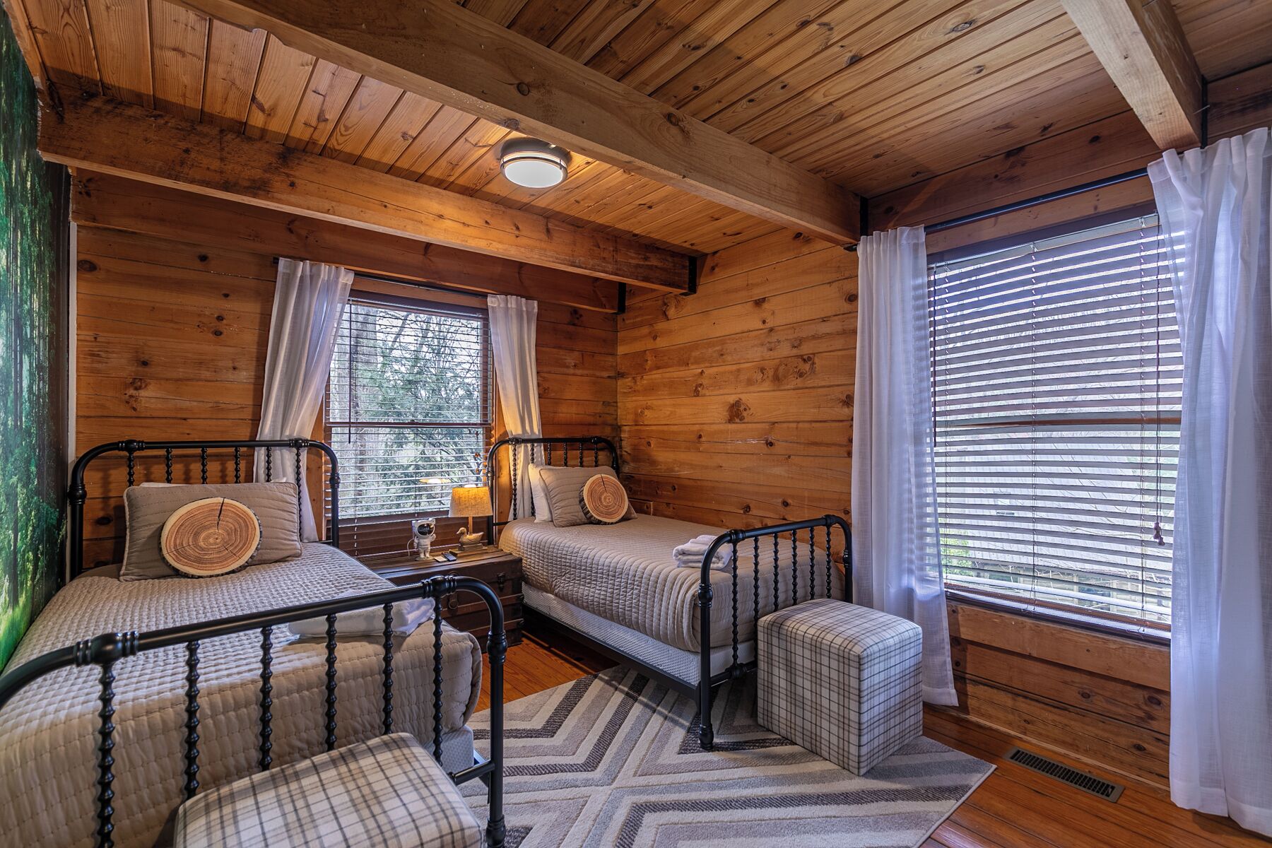 Une chambre de style cabane avec deux lits, une petite table et une fenêtre avec des stores.