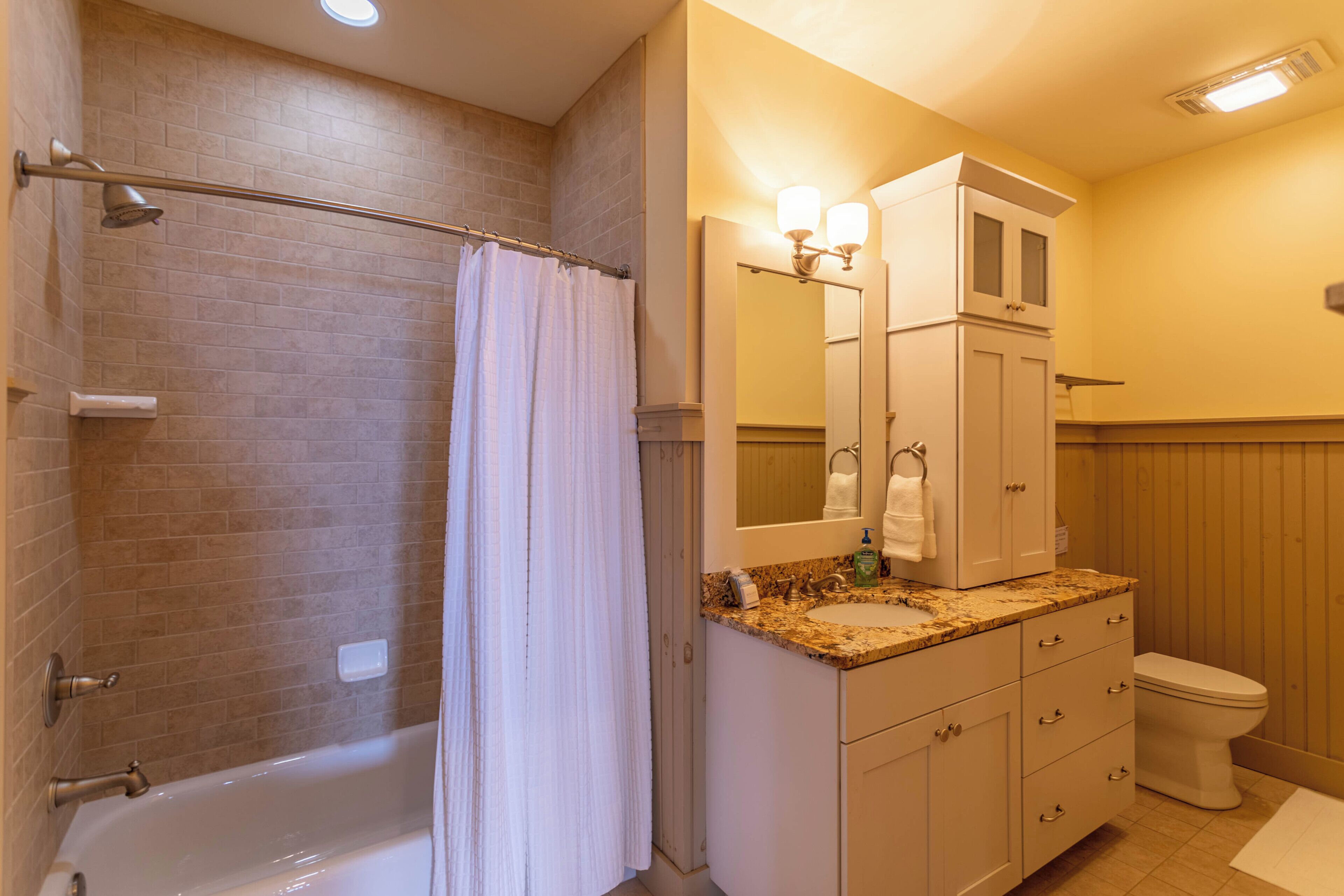 A bathroom with a bathtub, a shower curtain, a sink with a mirror, and a toilet.