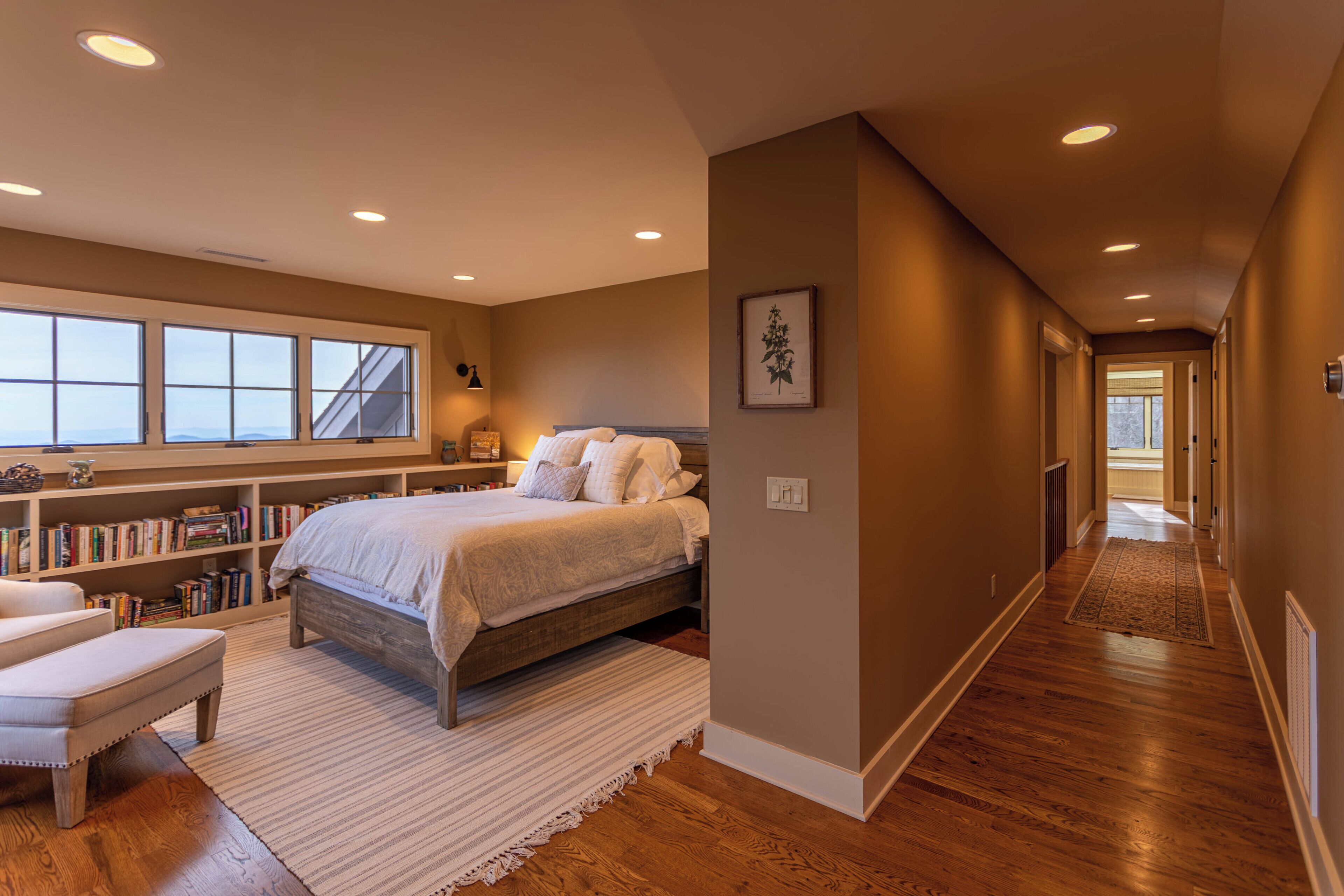 A bedroom with a large bed, a bedside table, a bookshelf, and a window.