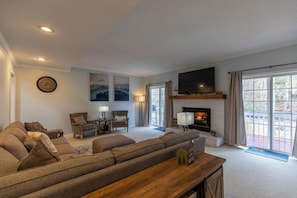 A living room with a sofa, armchairs, a fireplace, a television, and a large window. - Riverwood at Mill Ridge (Banner Elk)