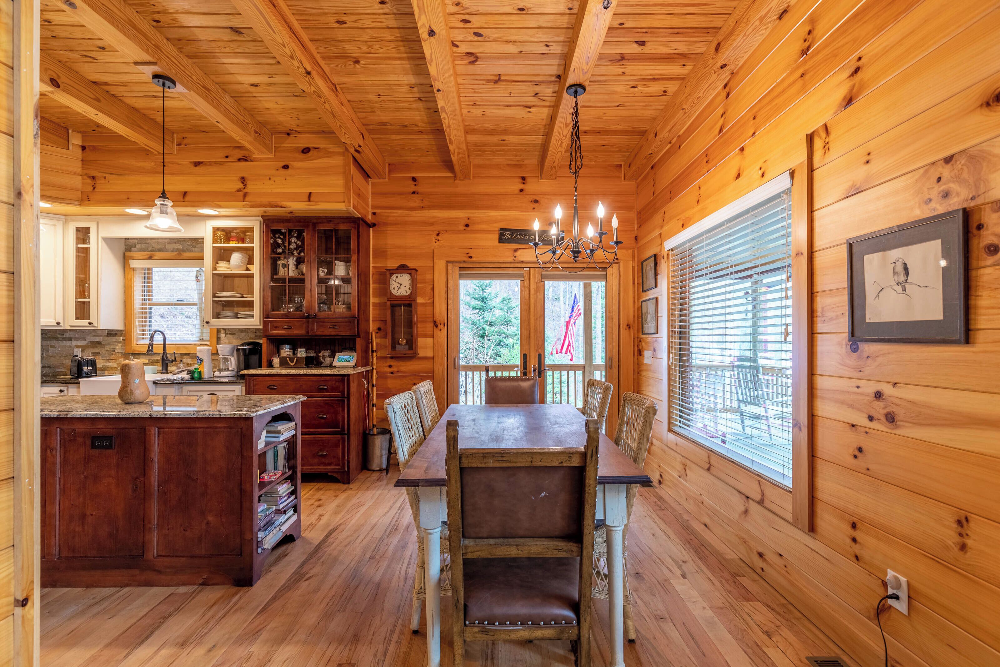 A wooden cabin interior with a dining area, kitchen, and a large window with blinds.
