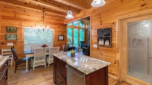 A wooden cabin interior with a kitchen area featuring a granite countertop, a dining table with chairs, and a refrigerator.