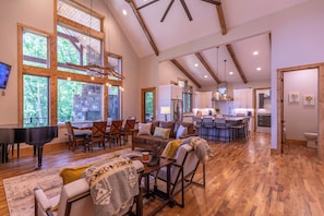 A spacious living room with a grand piano, a cozy seating area, and a kitchen in the background. - The Recovery Room at Eagles Nest (Banner Elk)