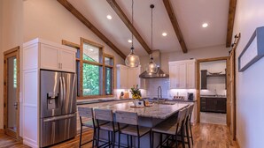 A modern kitchen with a central island, stainless steel appliances, and wooden beams on the ceiling. - The Recovery Room at Eagles Nest (Banner Elk)