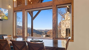 A dining area with a large table and chairs, large windows with a view of mountains and a stone building. - The Recovery Room at Eagles Nest (Banner Elk)