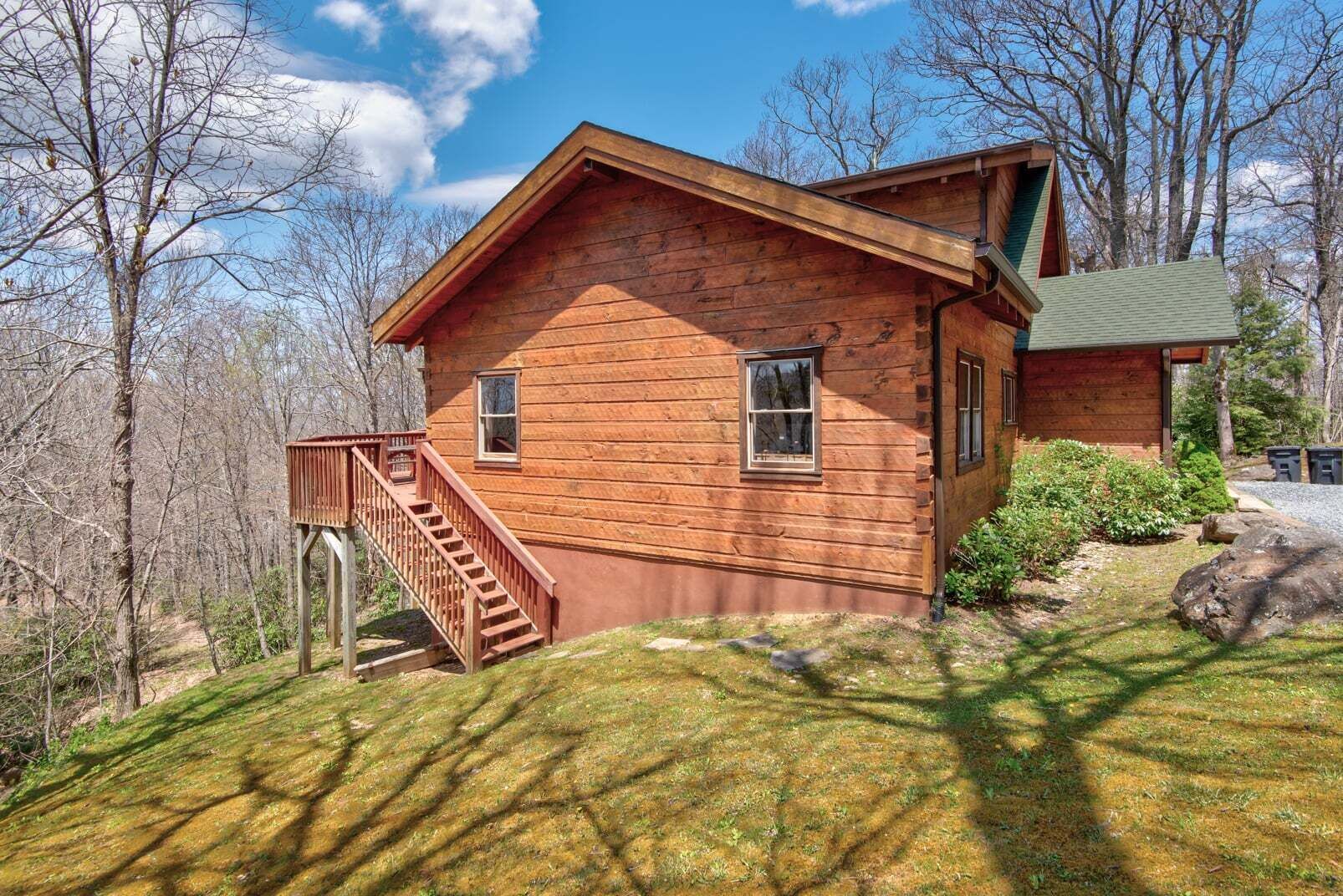 A wooden cabin with a staircase leading to a deck, surrounded by trees.