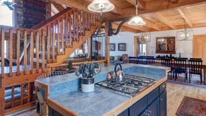 A spacious kitchen with a large island, wooden beams, and a rustic staircase. - Boles Lodge (Boone)