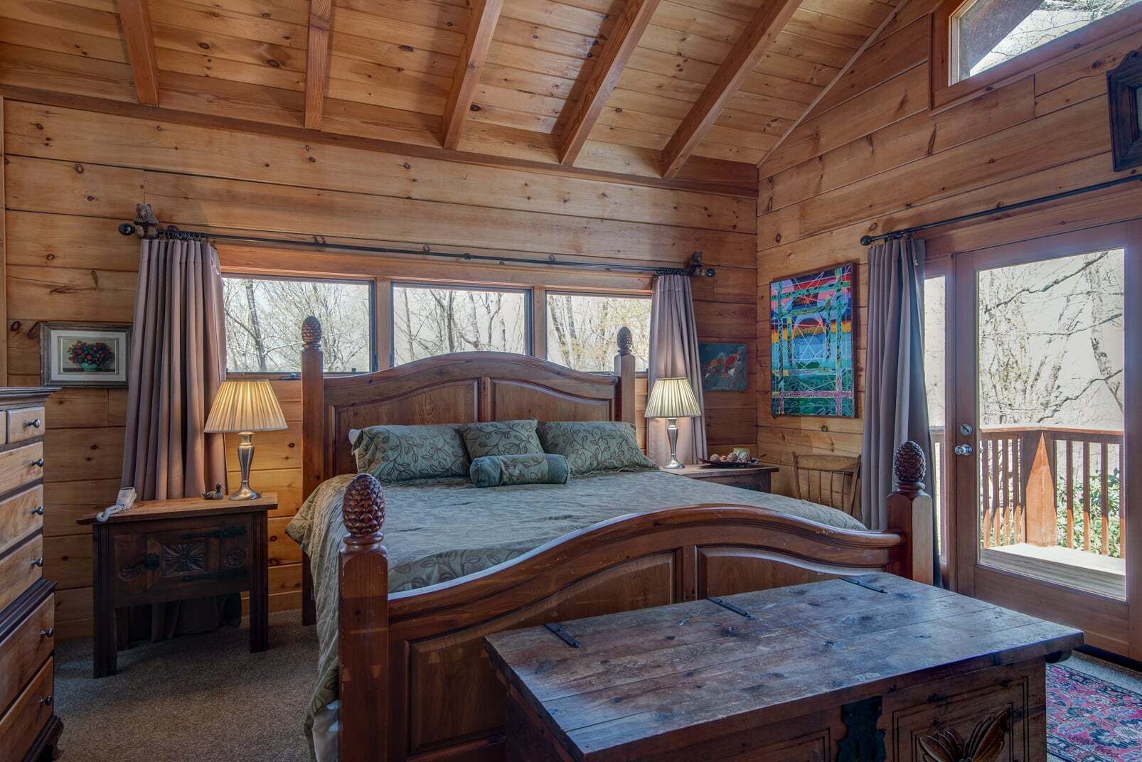A wooden cabin bedroom with a bed, bedside tables, a window, and a view of trees.