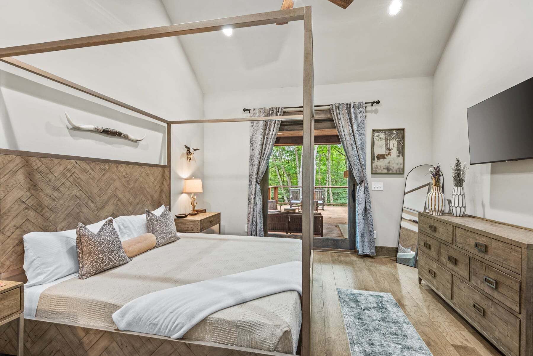 A bedroom with a four-poster bed, a wooden headboard, a nightstand, a dresser, a mirror, and a TV.