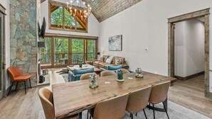 A spacious interior with a large dining table, comfortable seating, and a stone wall. - Streamsong at Eagles Nest (Banner Elk)