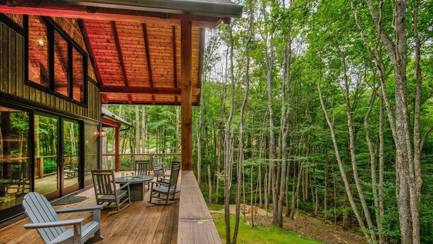 A wooden deck with outdoor furniture, a glass door leading to a deck, and a forested backdrop. - Streamsong at Eagles Nest (Banner Elk)