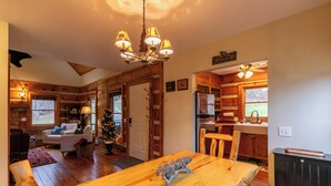 A cozy cabin interior with a dining table, wooden walls, a chandelier, and a kitchen area. - Valle Creek Cabin (Vilas)