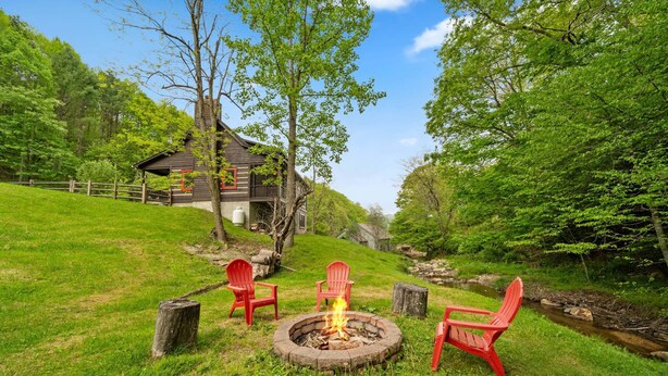 A rustic cabin with a fire pit and red chairs in a lush green setting. - Valle Creek Cabin (Vilas)