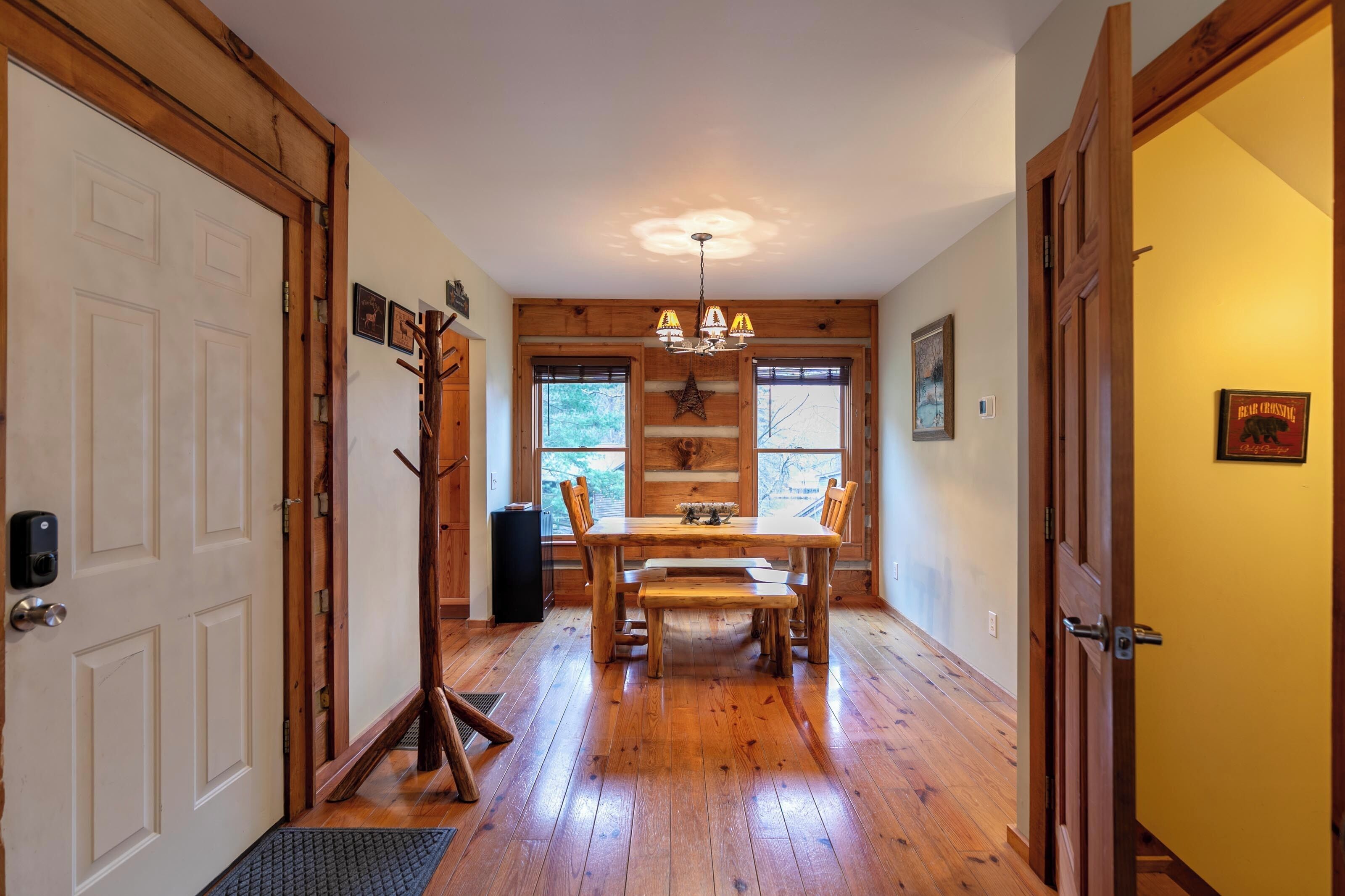 Un interior de madera con una mesa de comedor, sillas, un banco, una araña y una puerta con cerradura electrónica.