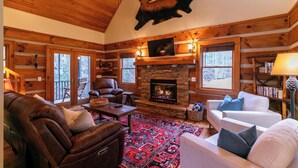A log cabin interior with a fireplace, leather recliner, white sofa, and a ceiling fan. - Valle Creek Cabin (Vilas)