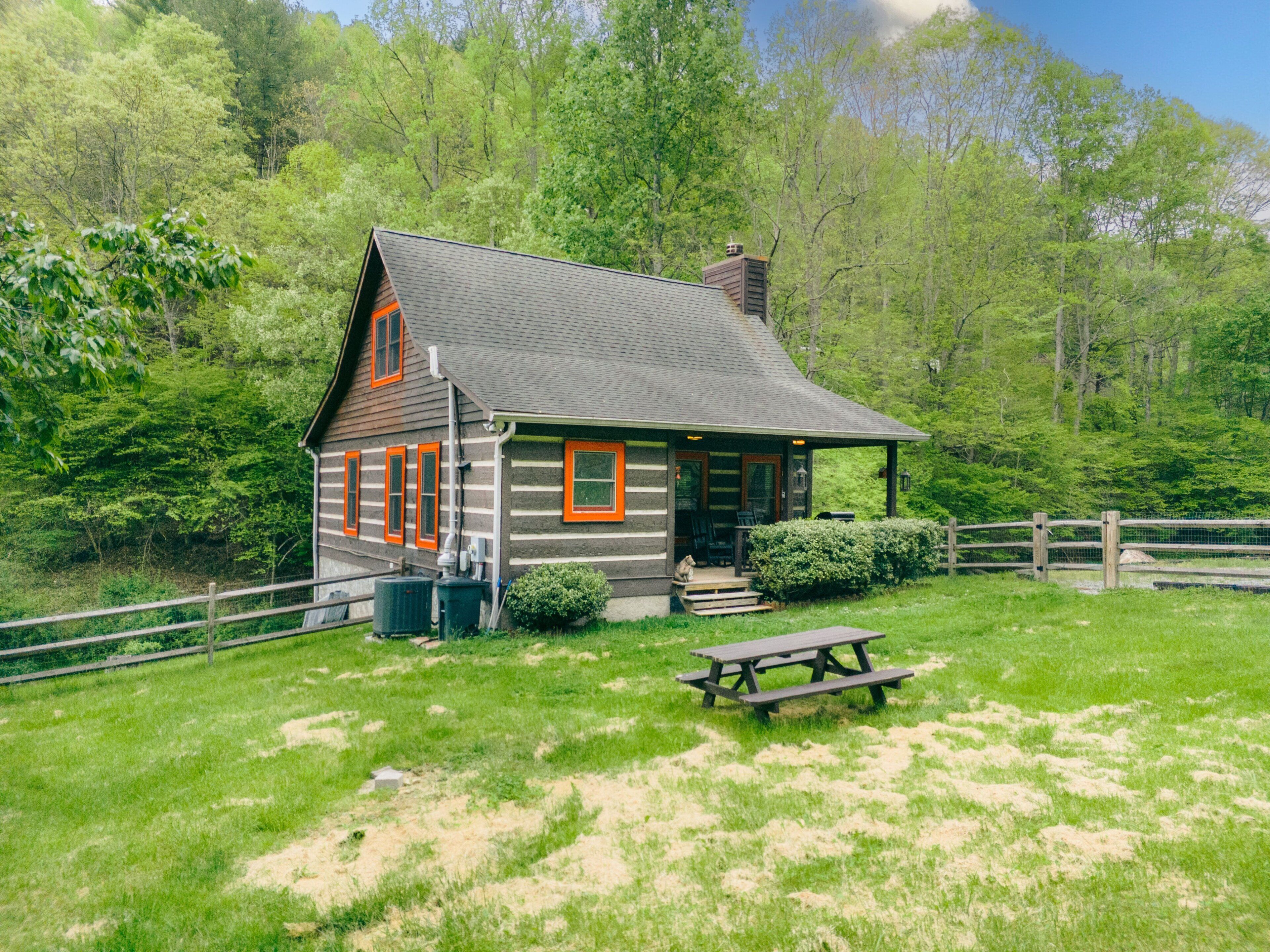 Eine Blockhütte mit Veranda und Picknicktisch in einer grünen, von Bäumen umgebenen Umgebung.