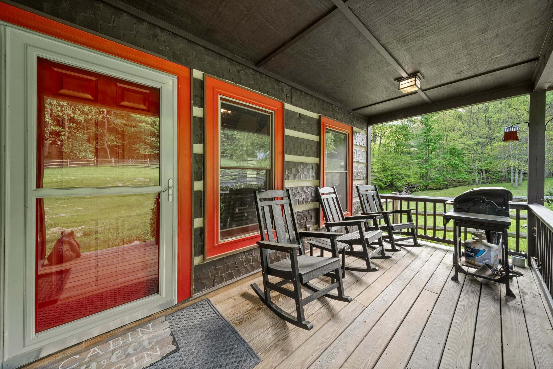 Een overdekt terras met schommelstoelen, een barbecue en uitzicht op een gazon.