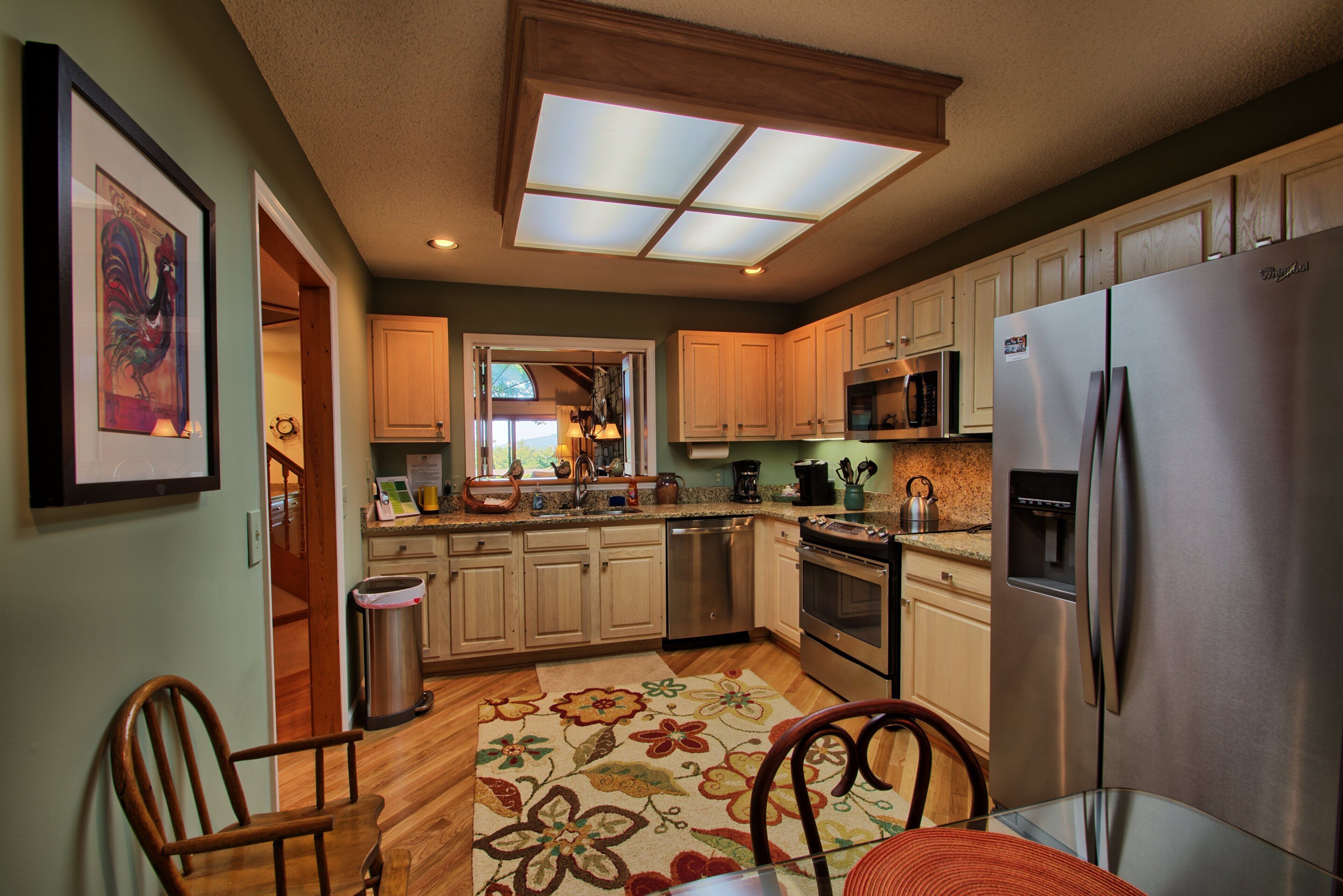 A kitchen with wooden cabinets, a stainless steel refrigerator, and a large window with skylight.
