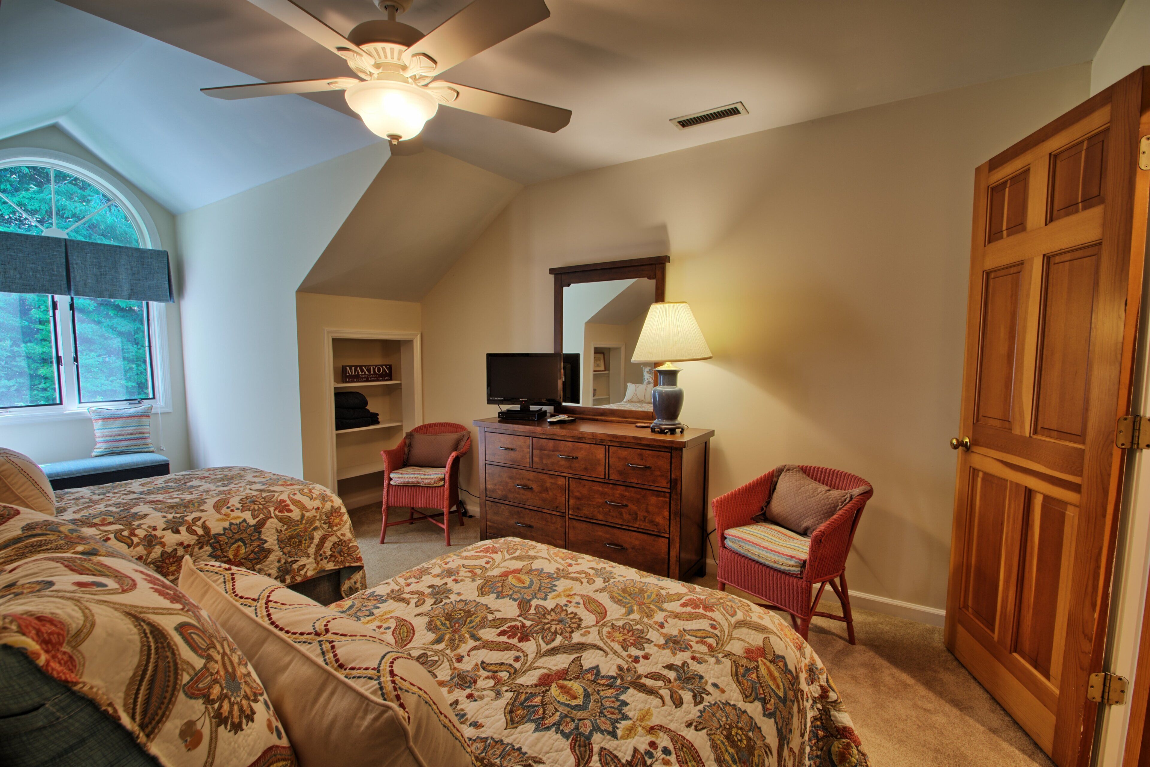 A bedroom with two beds, a ceiling fan, a dresser, a television, and a door.
