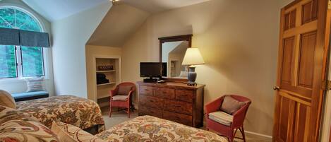 A bedroom with two beds, a ceiling fan, a dresser, a television, and a door.