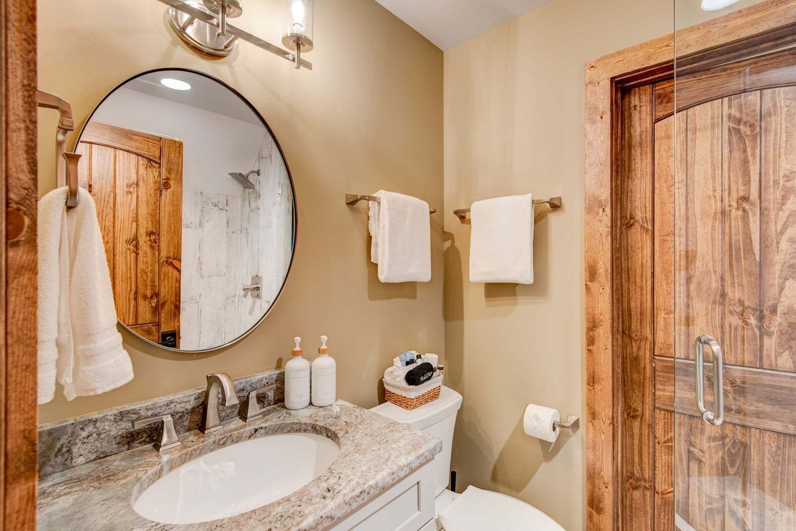 A bathroom with a round mirror, a sink, a toilet, and wooden paneling.
