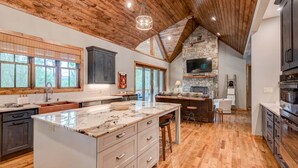A spacious kitchen with a large island, wooden ceiling, stone fireplace, and a stone wall TV. - High Country Hideaway at Eagles Nest (Banner Elk)