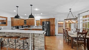 Uma cozinha ampla com armários de madeira, uma ilha central com banquetas, eletrodomésticos de aço inoxidável e iluminação pendente.