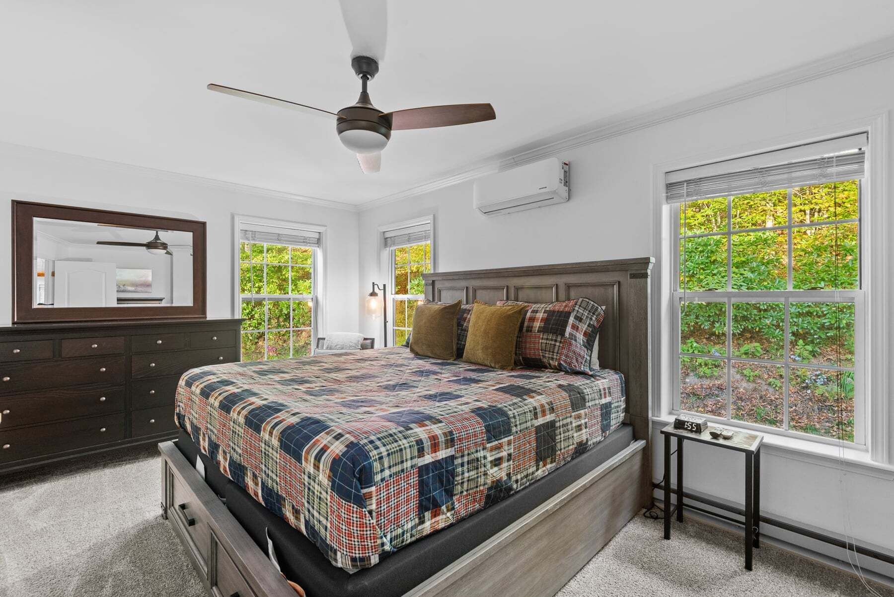 Une chambre à coucher comprenant un lit, une commode, un ventilateur de plafond, de grandes fenêtres et une vue sur la verdure.