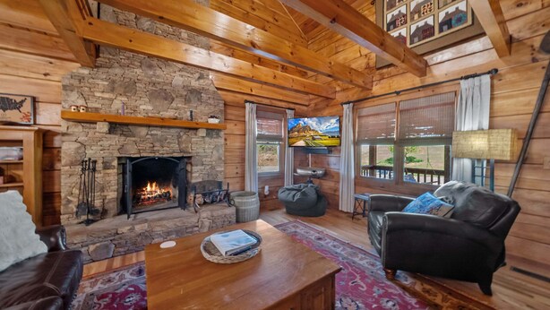 Un interior de cabaña acogedor con chimenea de piedra, vigas de madera, un sofá de cuero y un televisor.