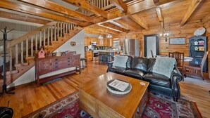 Un interior de madera con una escalera, una sala de estar con sofá de cuero, un comedor y una cocina.